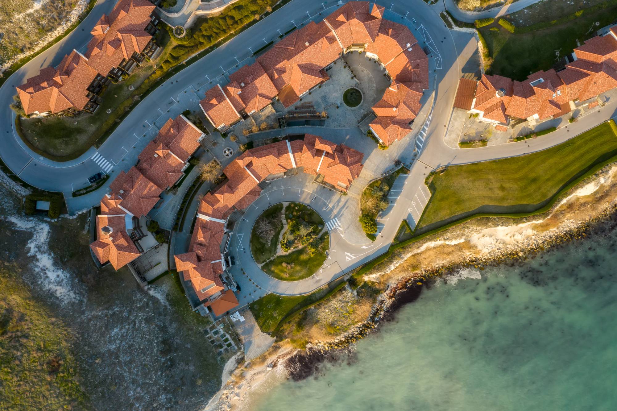 Aerial view of coastal homes with terracotta roofs above the sea at sunset