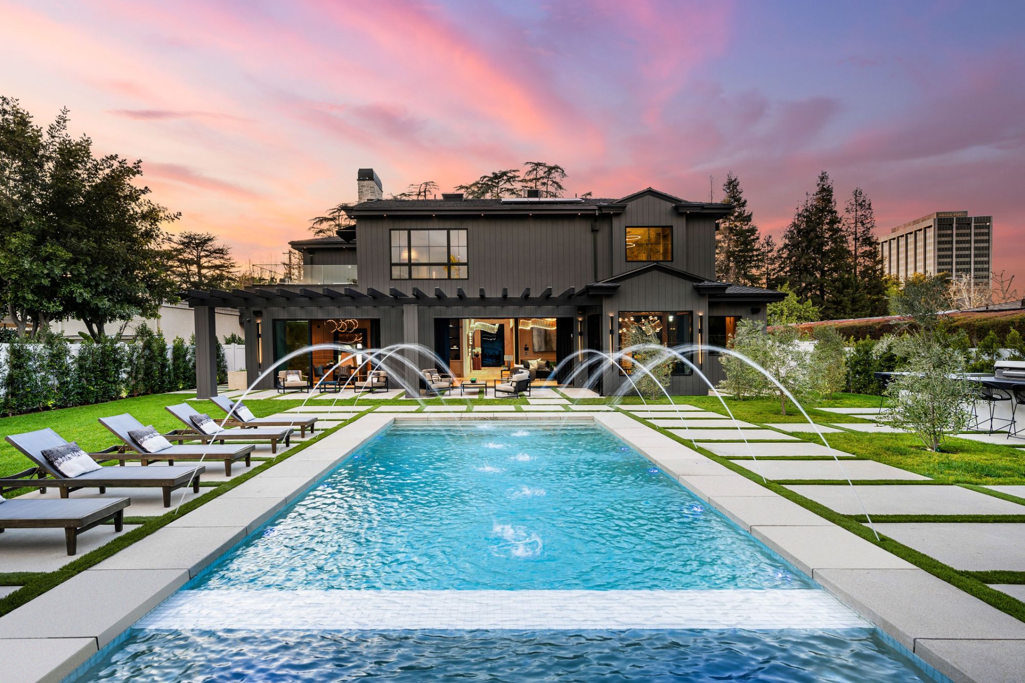 Dark modern farmhouse with a pool and fountains at sunset
