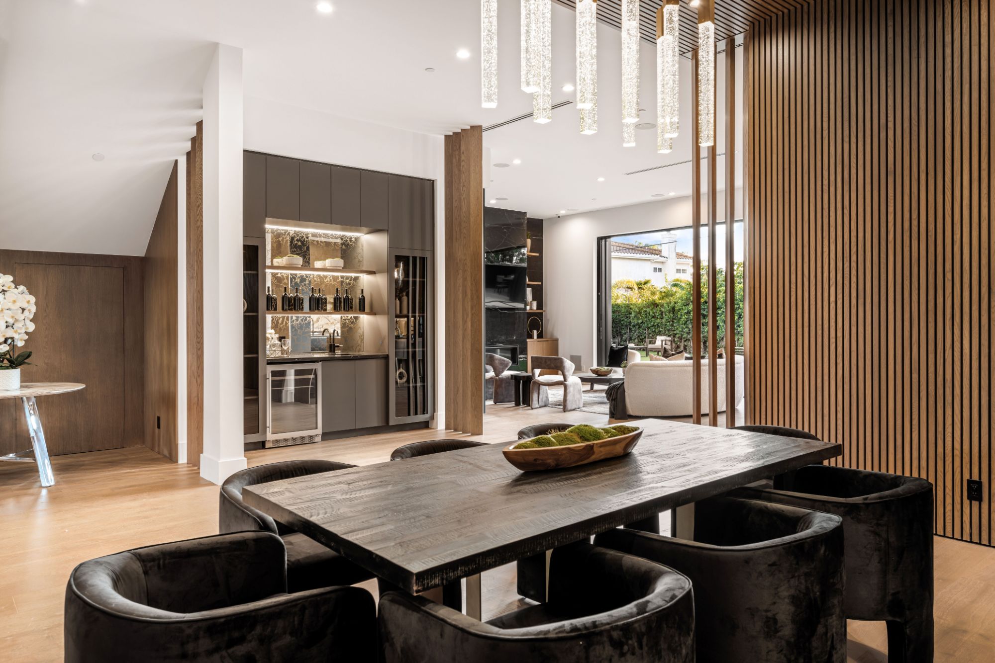 Dining room with velvet chairs, crystal pendants, and a slatted oak wall