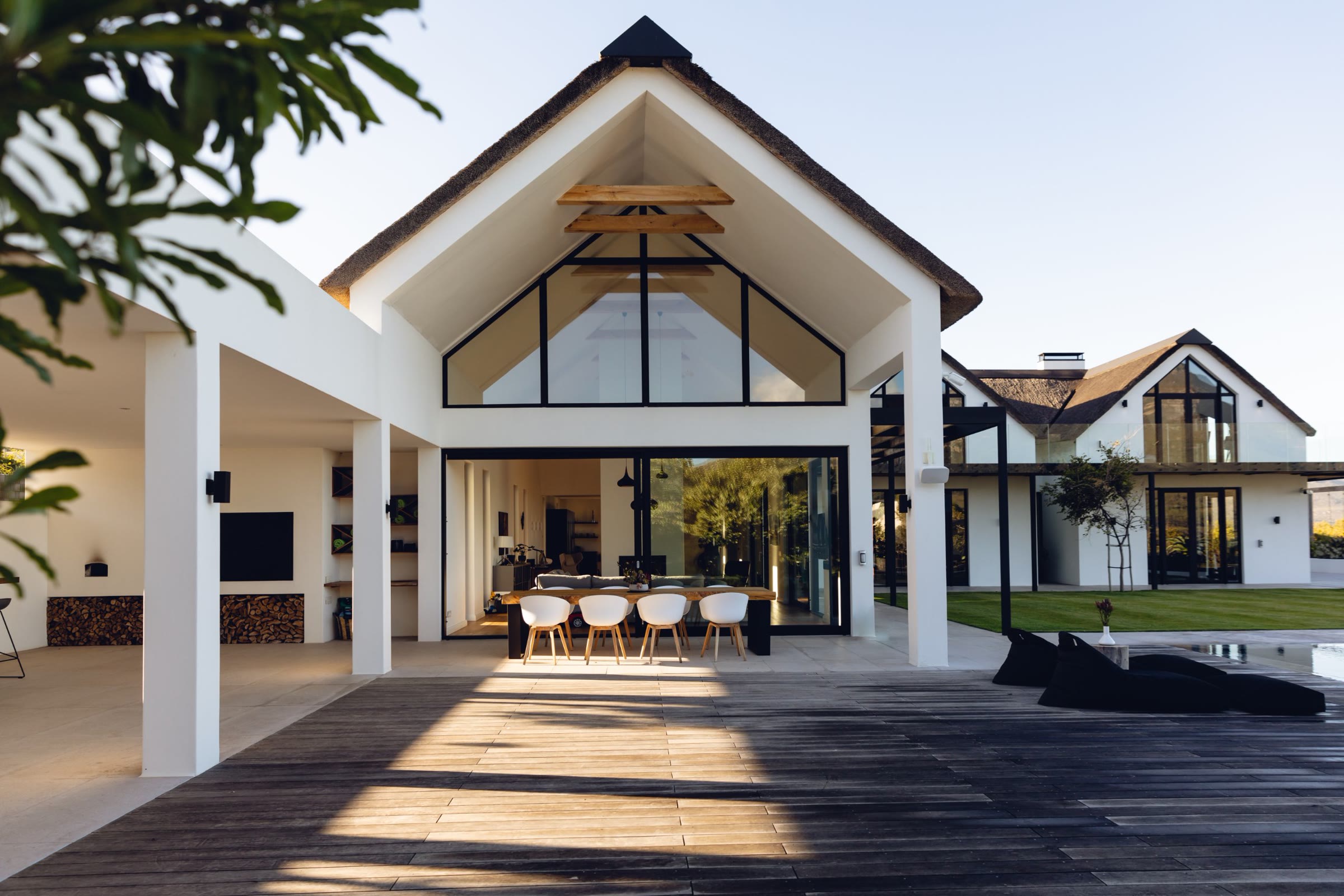 Gabled white house opening onto a timber deck in late sun