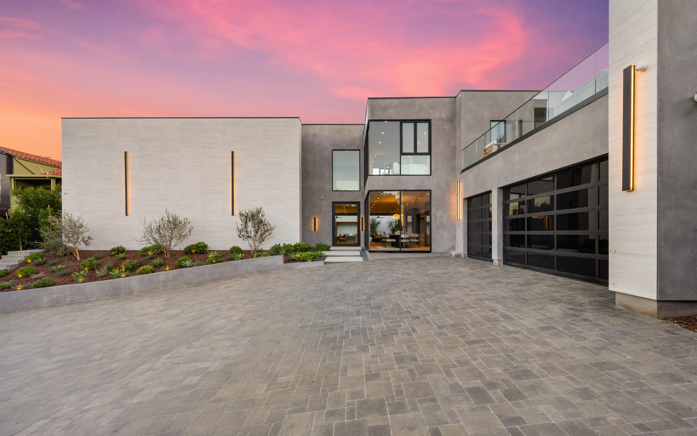 Modern stone and stucco home with a paved motor court at sunset