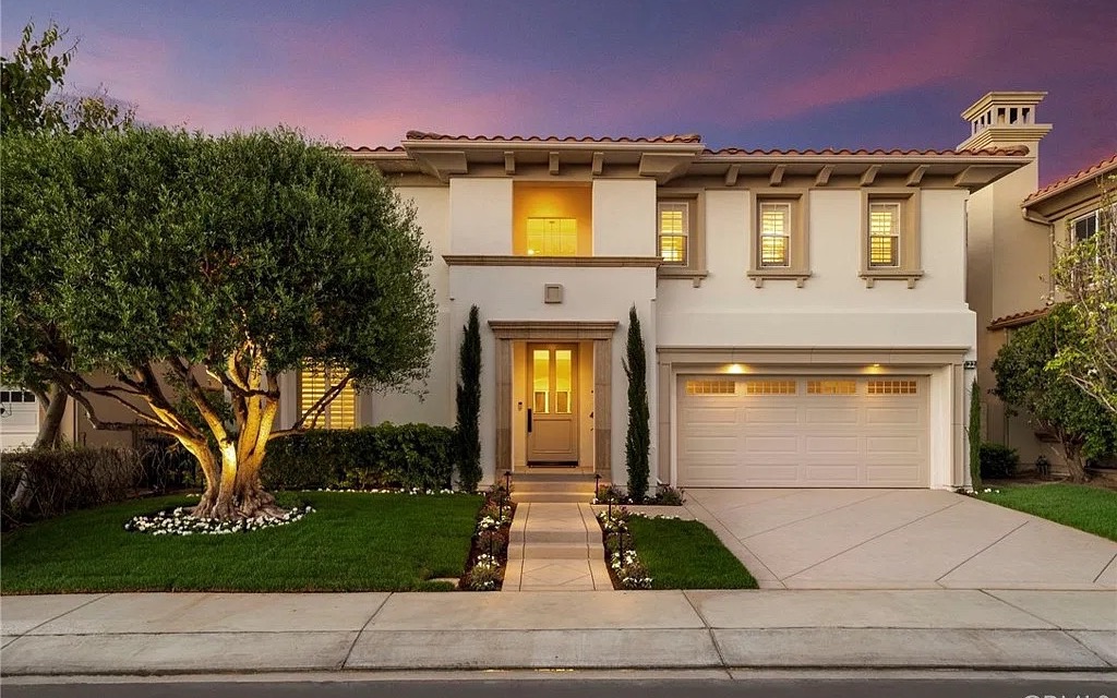 Two-storey home with a lit olive tree in the front garden at dusk