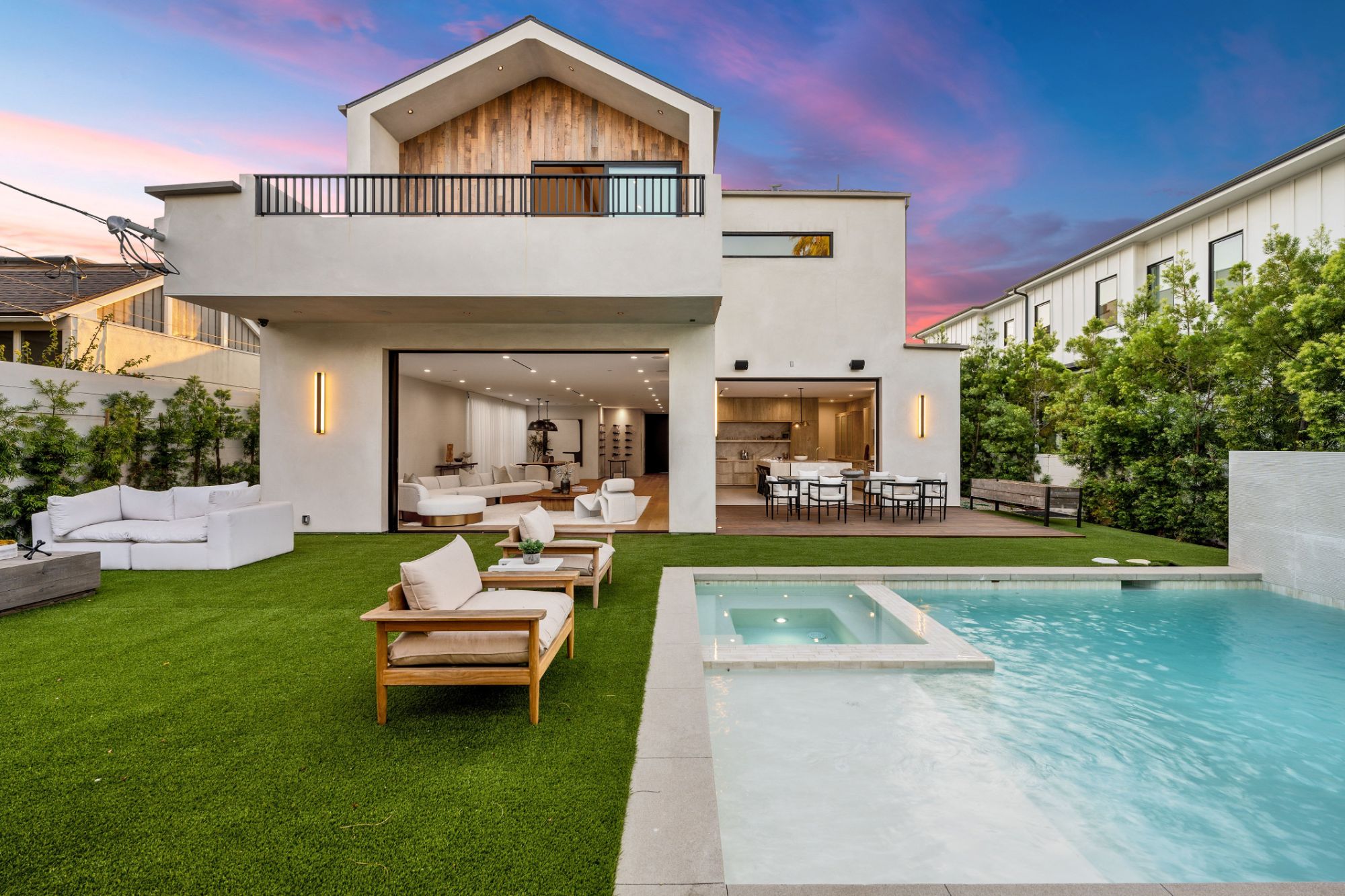 White modern home with a timber gable, lawn, and pool at dusk